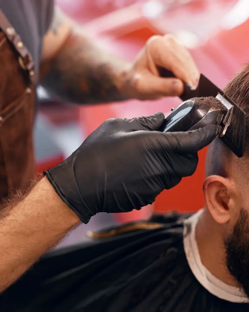 Barber in a leather apron and gloves cutting hair clipper over comb