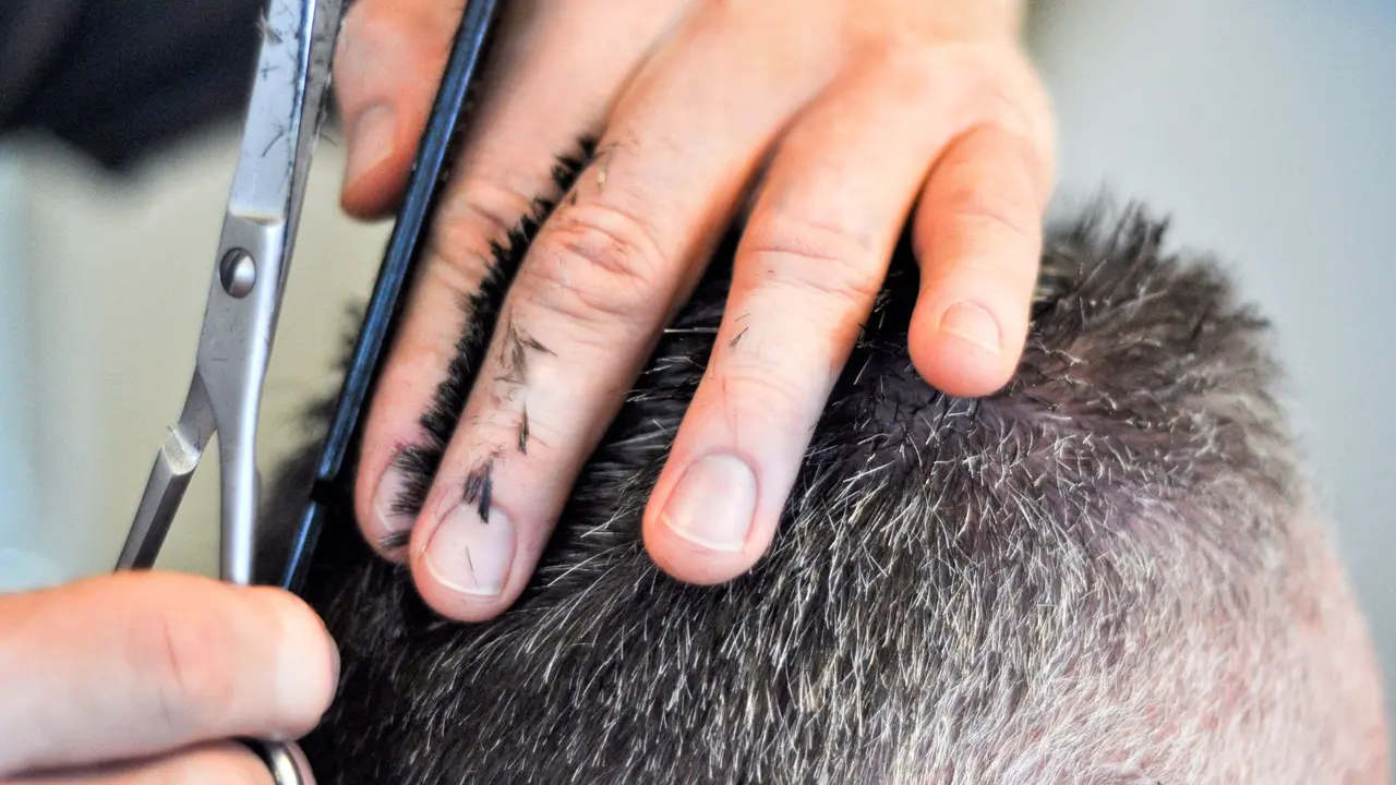 Barber cutting gray hair with scissors over fingers