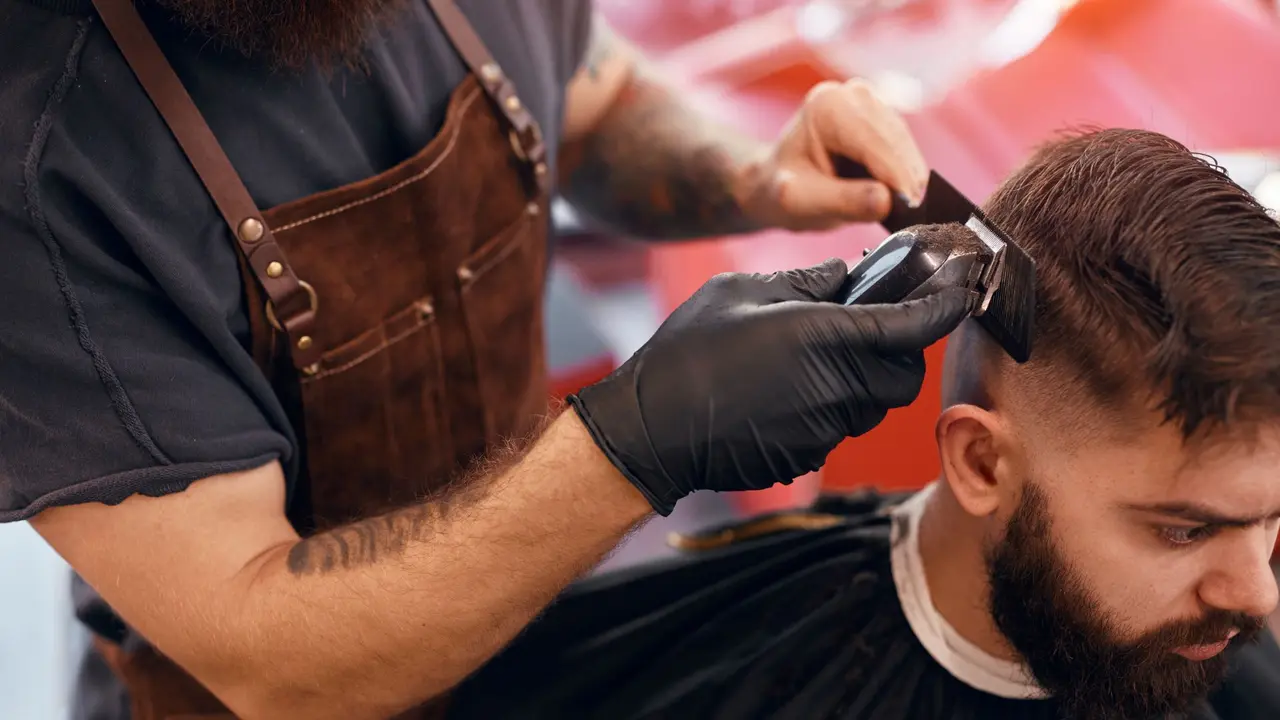 Barber in a leather apron cutting hair with clippers