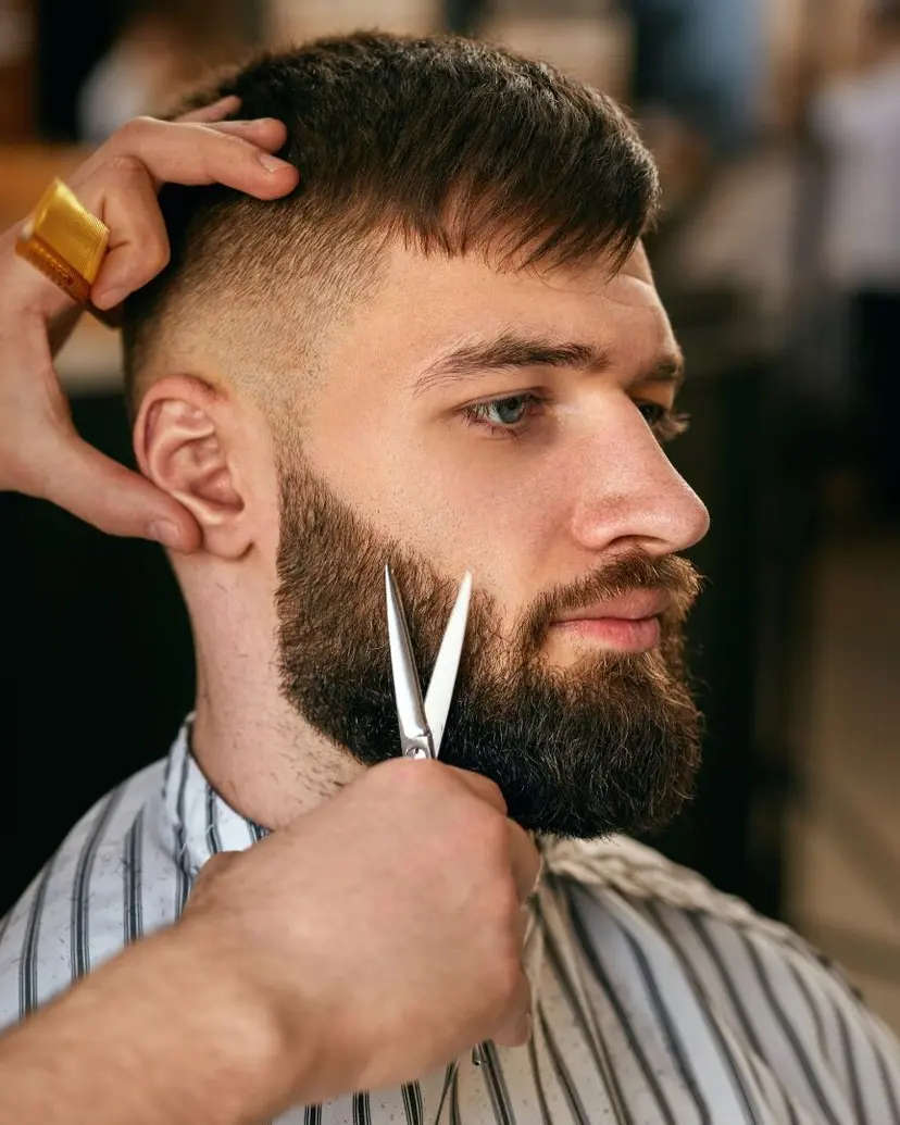 Barber trimming a full beard with scissors at a barber shop