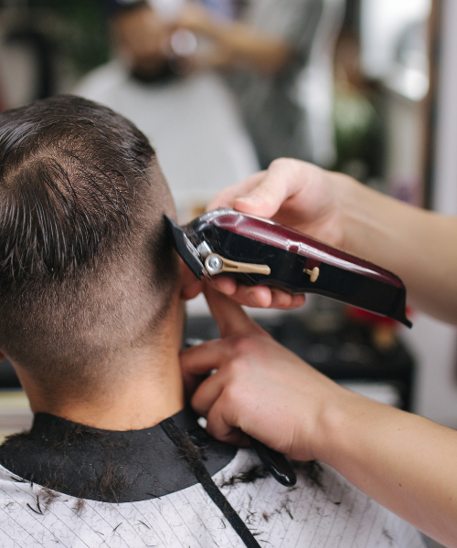 A man cutting another mans hair with a cell phone