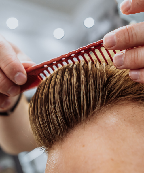 A person cutting another persons hair with a red comb